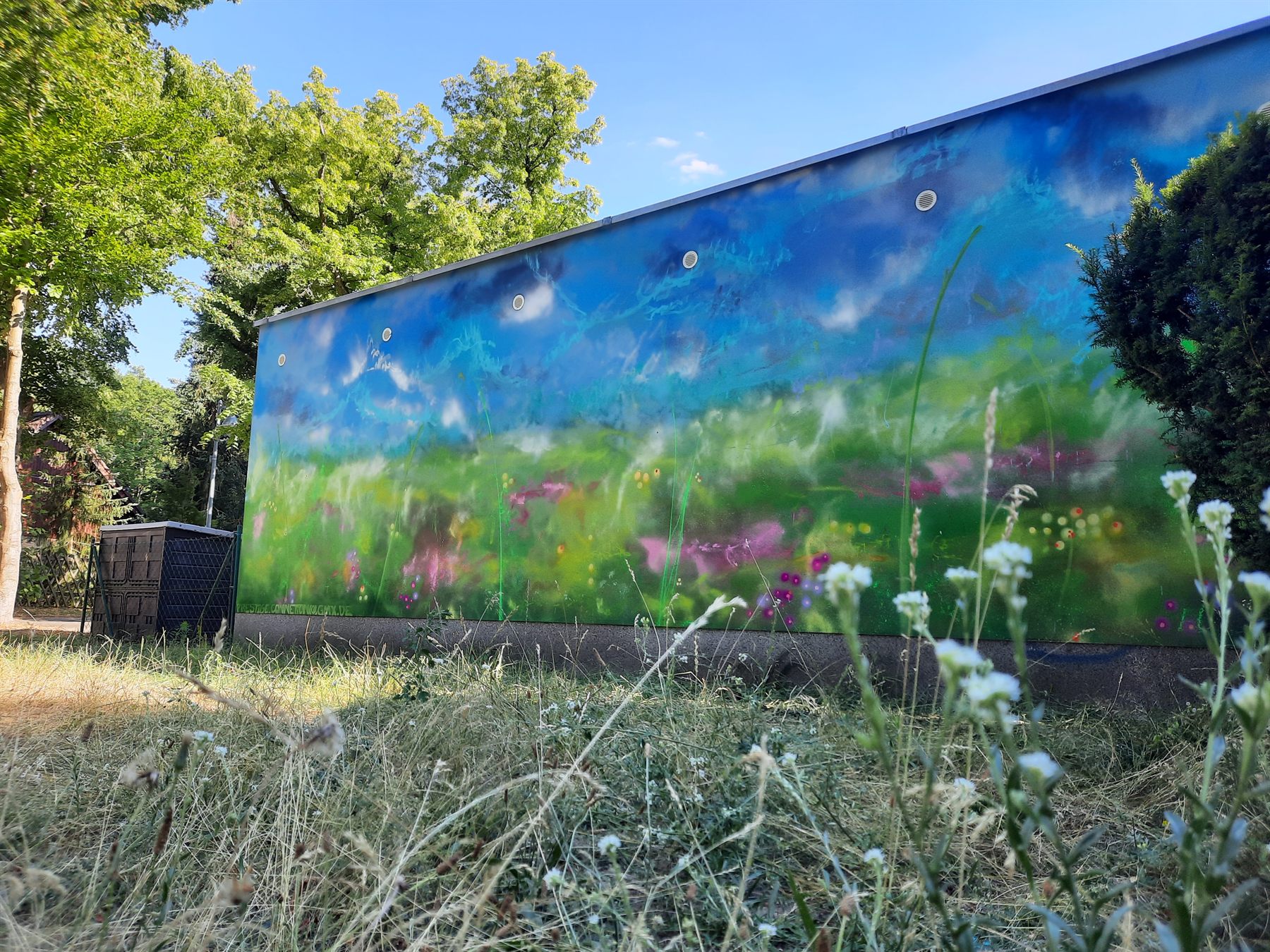Großflächiges Wandbild einer blühenden Wiese unter blauem Himmel an einer Gebäudefassade